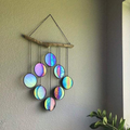 Rainbow hanging wall art decoration with circular reflective pendants and natural wood branch on a wall.